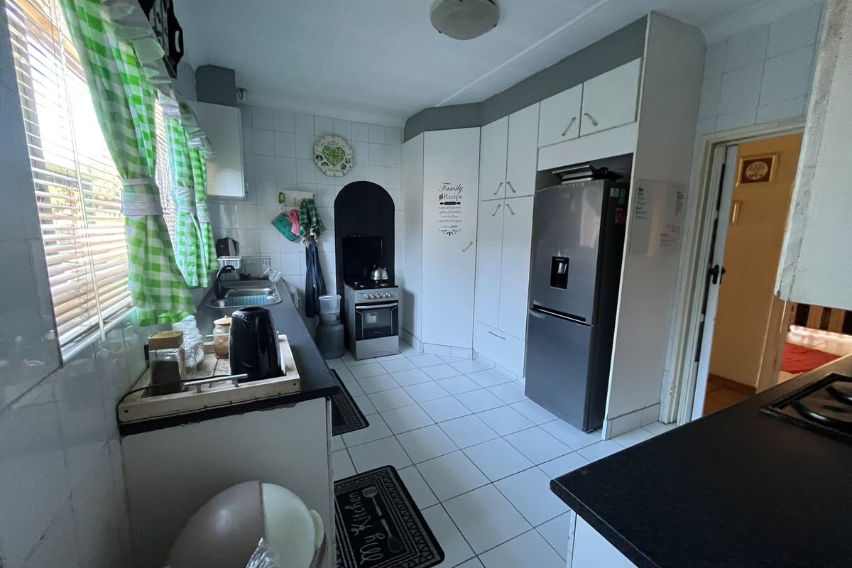 A functional kitchen featuring tiled flooring, white cabinetry, a stainless steel sink, and a freestanding stove with a tiled splashback.