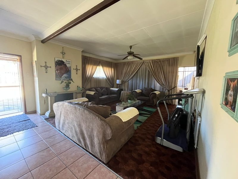 Spacious living room featuring a combination of tiled and carpeted flooring, a ceiling fan, and an exposed ceiling beam.
