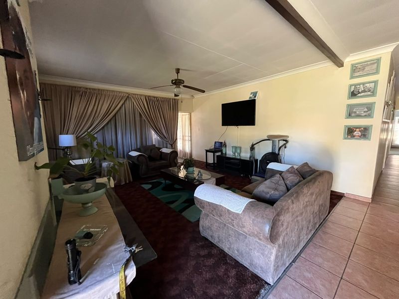 A spacious living room featuring a ceiling fan, exposed beam, and tiled flooring, offering a comfortable area for relaxation and entertainment.