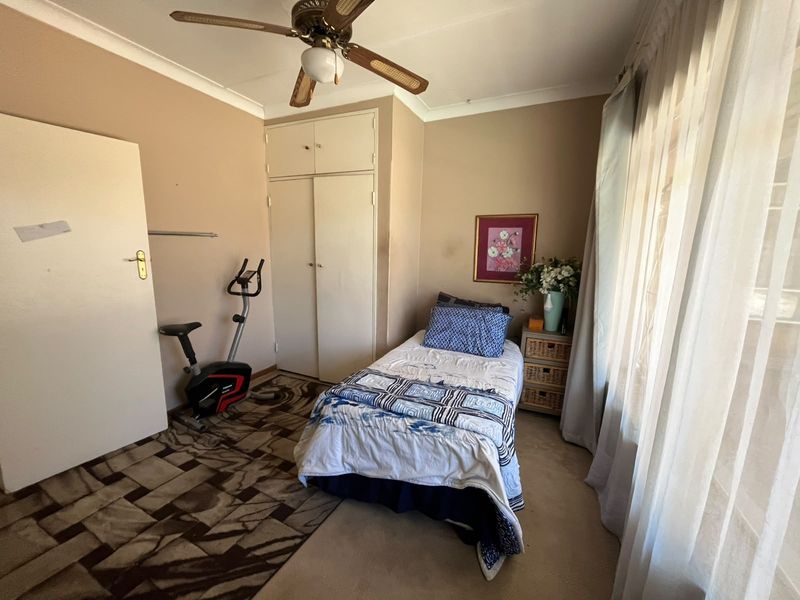 A bedroom featuring built-in cupboards, a ceiling fan, and large windows. The room requires cosmetic updates to the flooring and ceiling finishes.