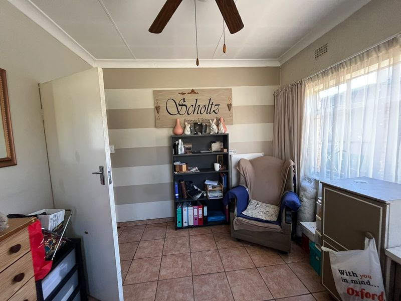 A bedroom featuring tiled flooring, a ceiling fan, and a window fitted with a security gate.