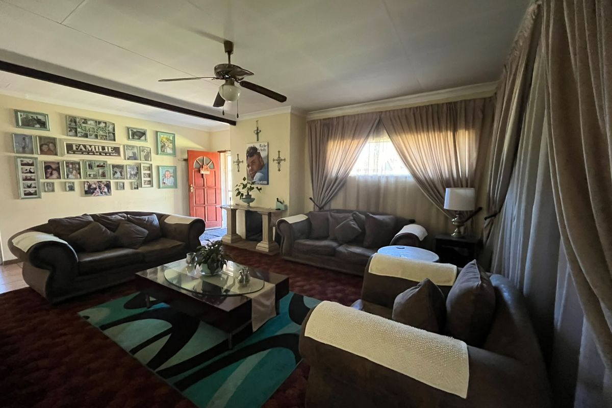 Spacious living room featuring a ceiling fan, exposed beam, and large windows with curtains, offering a traditional layout ready for modern updates.
