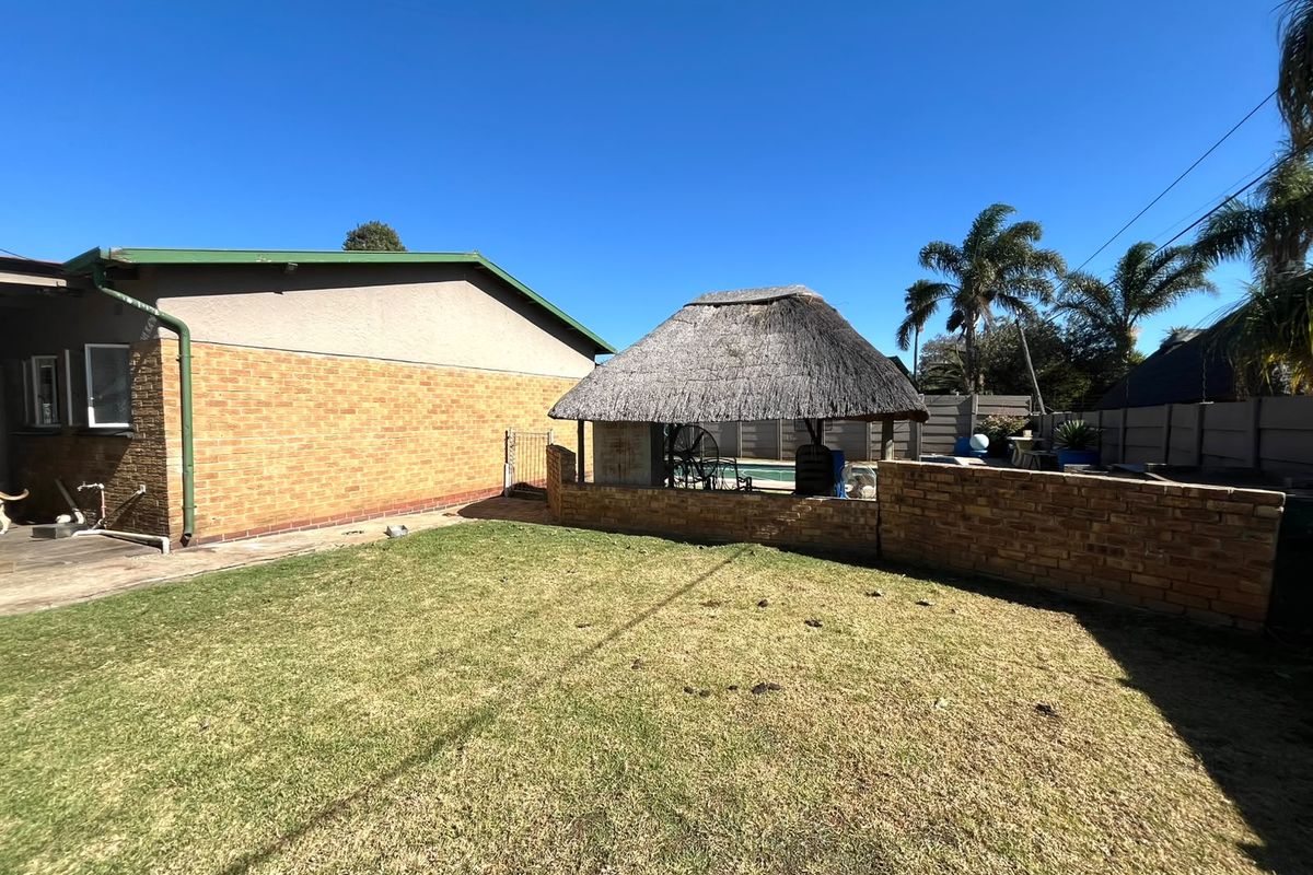 Rear garden featuring a brick facade house, a swimming pool, and a traditional thatched lapa entertainment area with a low brick boundary wall.