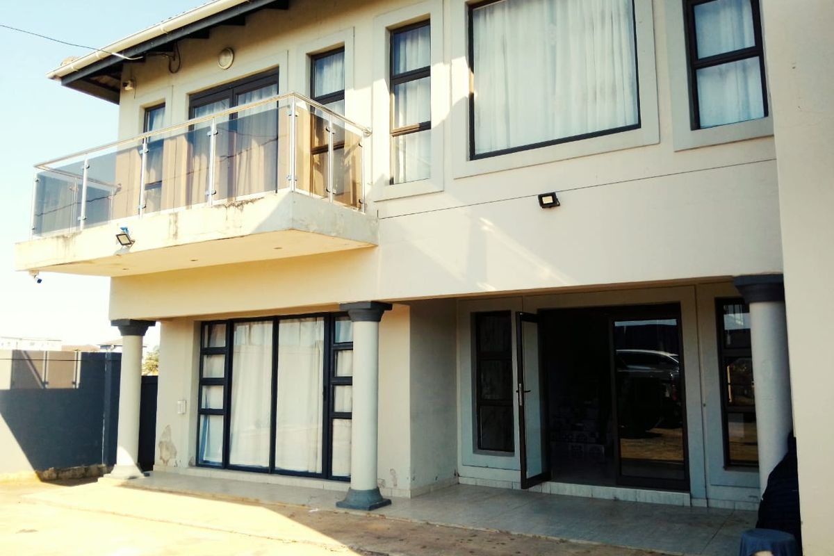 Rear elevation of a two-story house featuring a balcony with glass balustrade, tiled patio area, and sliding door access to the ground floor.