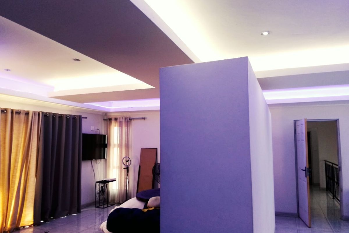 Spacious bedroom featuring a modern recessed ceiling with integrated cove lighting, tiled flooring, and a central partition wall.