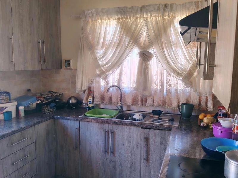 A functional kitchen featuring wood-look laminate cabinetry, dark countertops, a stainless steel sink, and a built-in hob with an extractor fan.