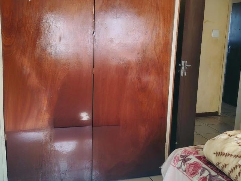 A bedroom featuring a large built-in wooden wardrobe and tiled flooring, showing signs of wear and dated finishes.