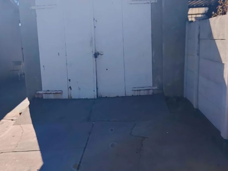 A detached garage featuring double doors and a concrete driveway, showing signs of wear and weathering on the exterior surfaces.