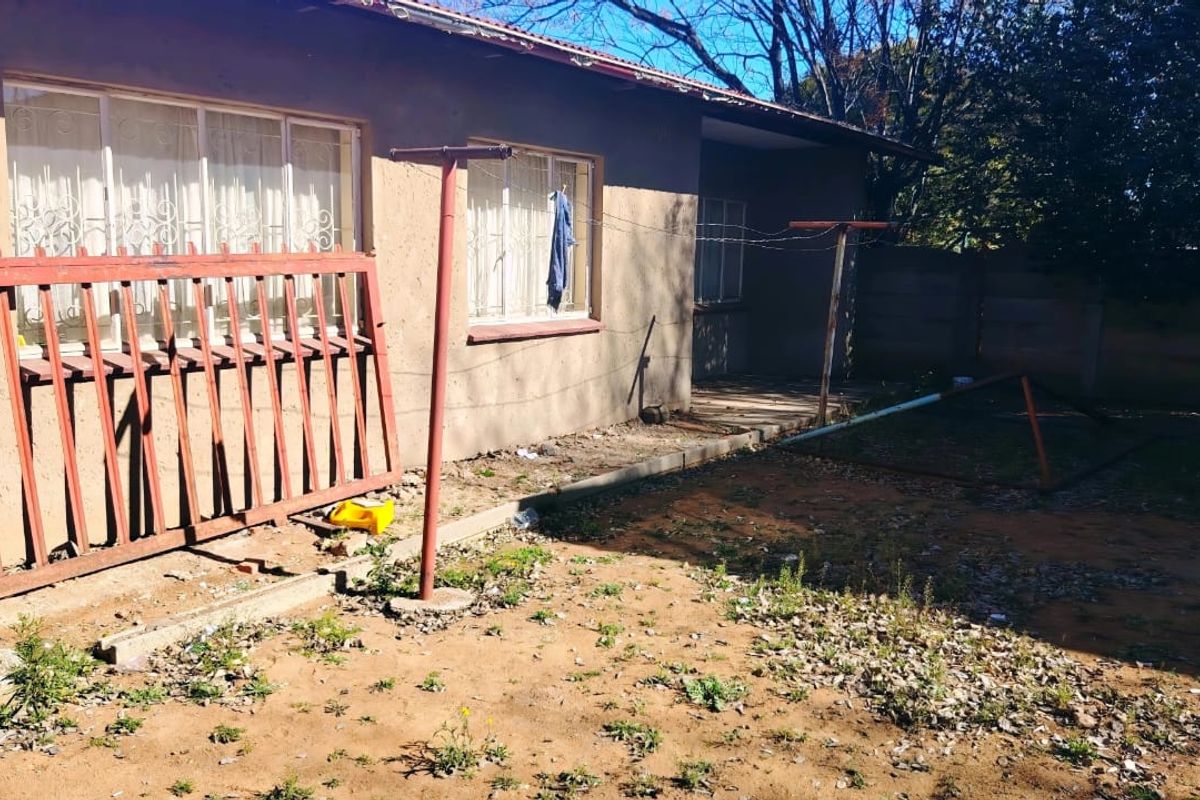 Rear exterior view of the property featuring a basic garden area, security bars on windows, and a metal washing line structure.