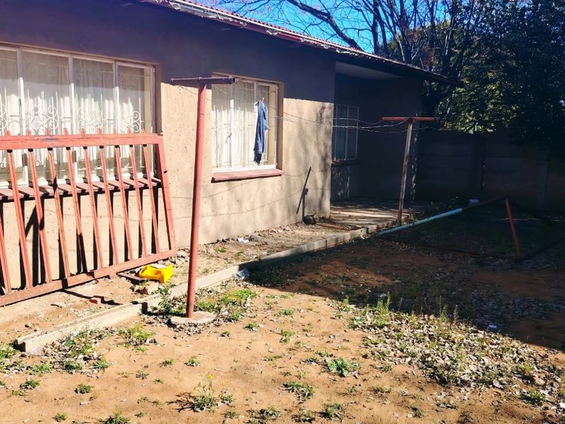 Rear exterior view of the property featuring a basic garden area, security bars on windows, and a metal washing line structure.