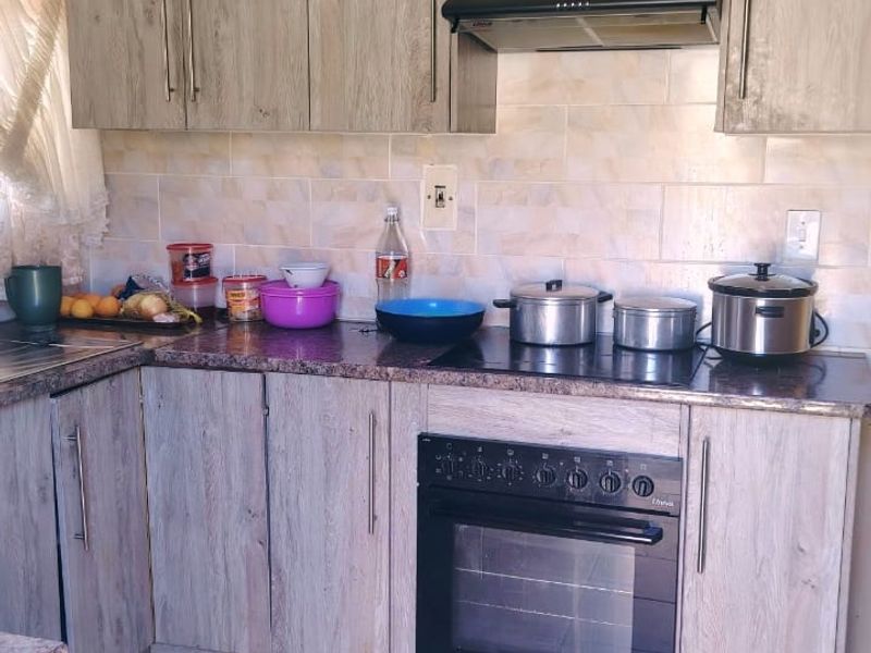 A functional kitchen featuring light wood-grain laminate cabinetry, granite countertops, a built-in oven with ceramic hob, and a tiled backsplash.