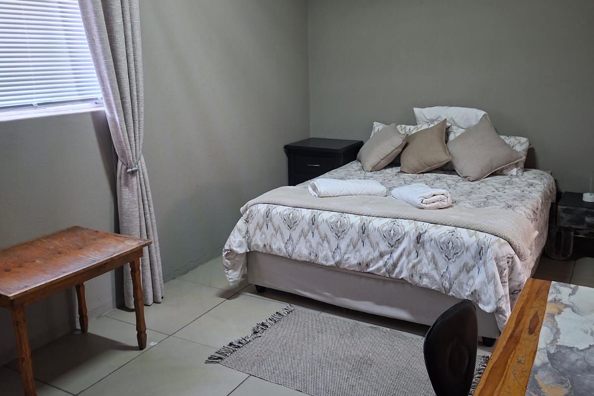 A functional bedroom featuring tiled flooring, neutral wall tones, and window treatments including blinds and curtains.