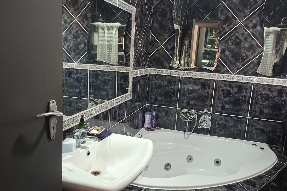 Bathroom featuring a corner spa bath, pedestal basin, and dark decorative wall tiling with integrated mirrors.