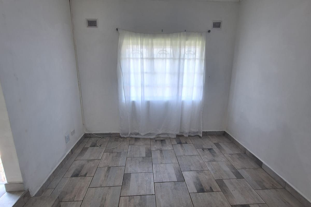 A vacant bedroom featuring wood-look tiled flooring, a window with security bars, and neutral white walls, offering a clean canvas for personalization.