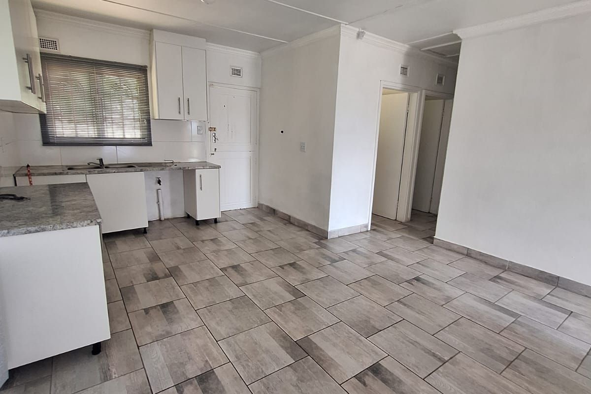 A clean, empty kitchen featuring neutral tiled flooring, white cabinetry, and laminate countertops, offering a blank canvas for potential buyers.