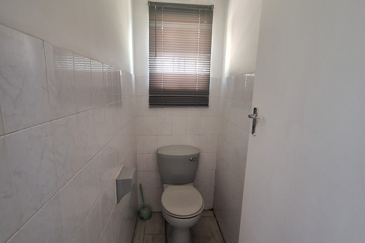 A compact, functional guest toilet featuring neutral wall tiles, wood-look floor tiles, and a window with a fitted blind.