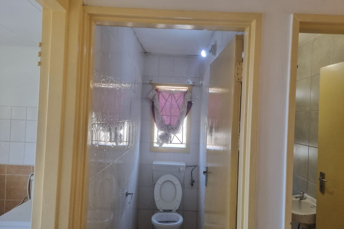 A compact bathroom featuring a toilet and pedestal basin with tiled walls, requiring cosmetic updates to modernize the space.