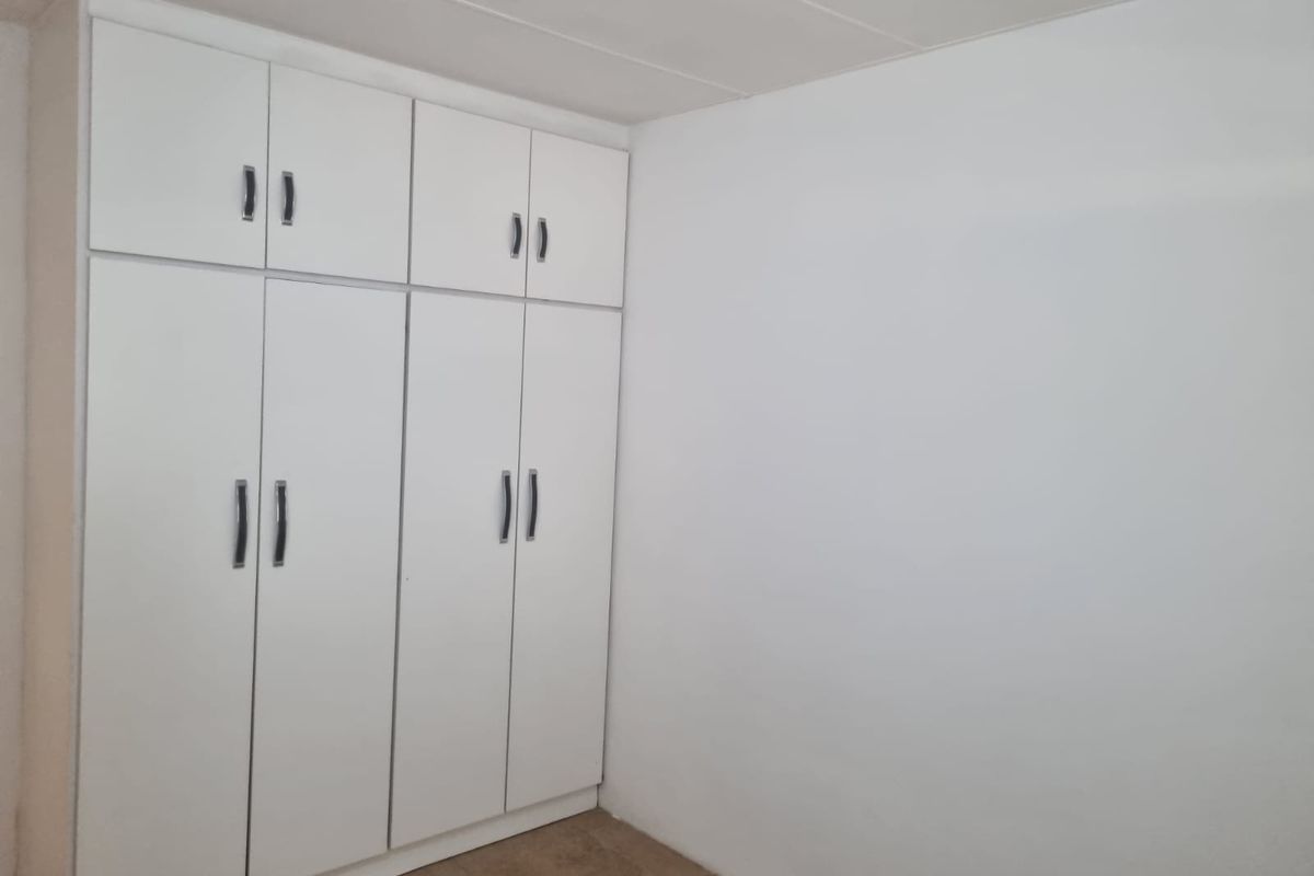 A clean, empty bedroom featuring white built-in cupboards with modern handles, providing ample storage space.
