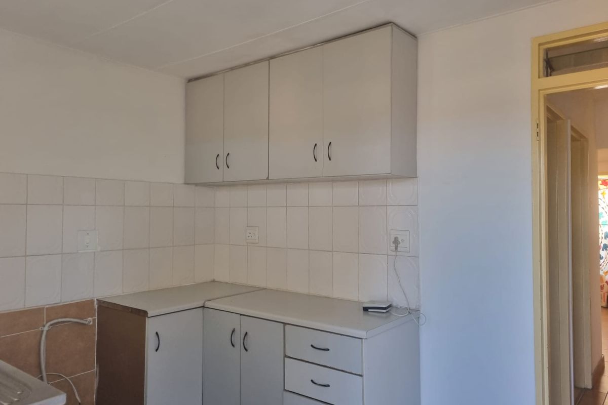 A compact kitchen area featuring basic laminate cabinetry, tiled splashbacks, and functional counter space, ready for modernization.