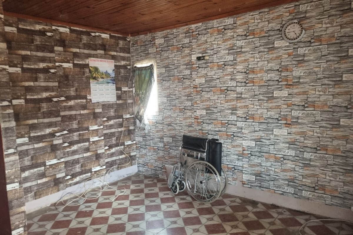 A bedroom space featuring timber ceiling paneling, patterned wallpaper, and tiled flooring, currently vacant and requiring cosmetic updates.