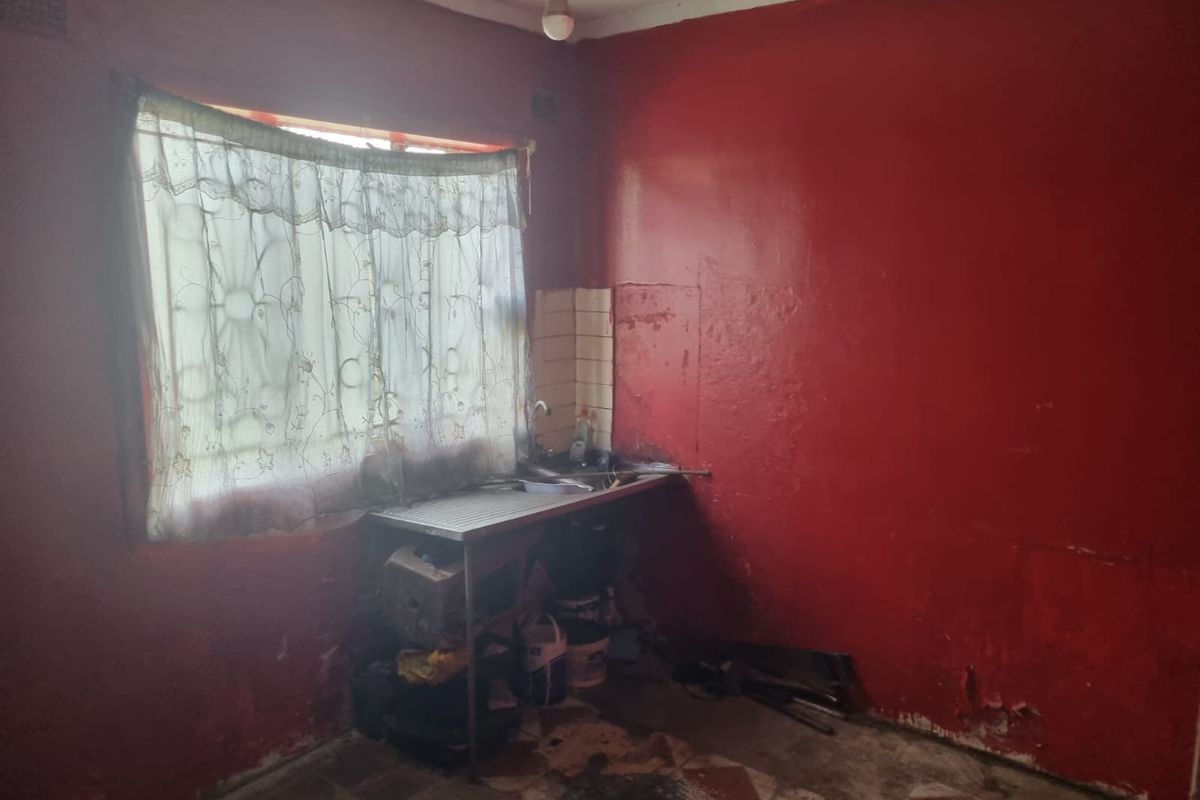 A basic kitchen area featuring a stainless steel sink, tiled splashback, and security bars on the window, requiring significant renovation and cosmetic updates.