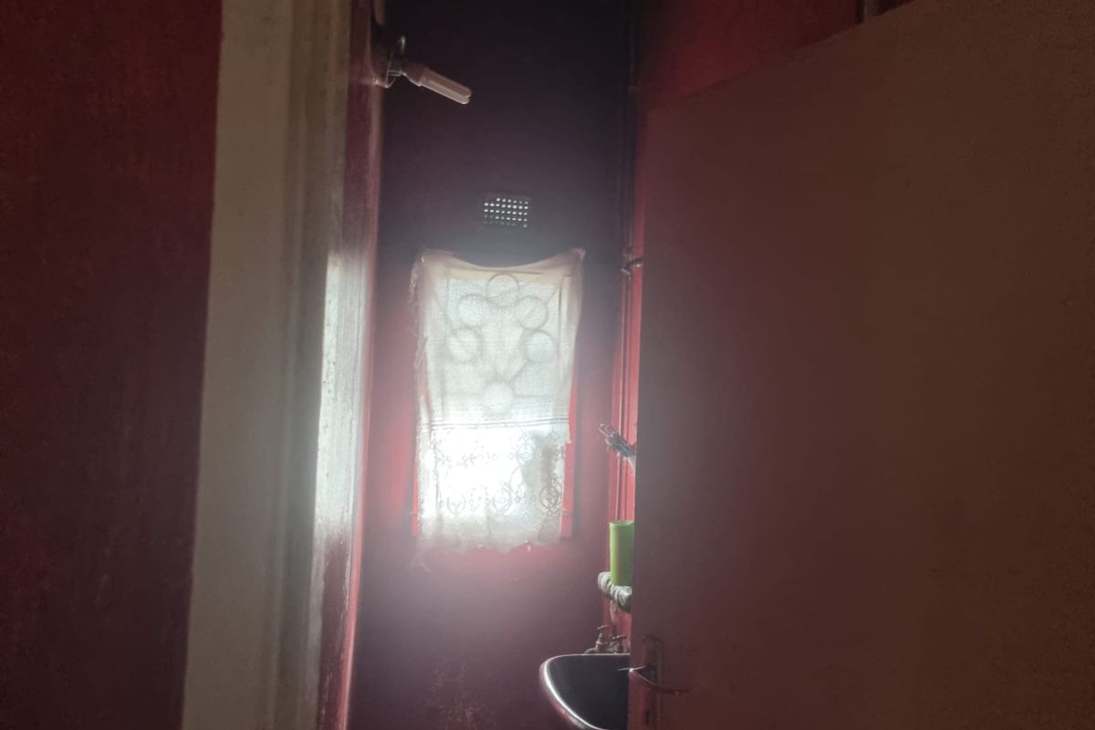 A small, dimly lit bathroom space featuring a wall-mounted basin and ventilation brick, requiring significant cosmetic updates and improved lighting.