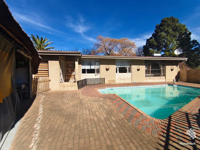 Rear exterior view featuring a swimming pool, brick paved patio area, and a covered outdoor structure under a clear blue sky.