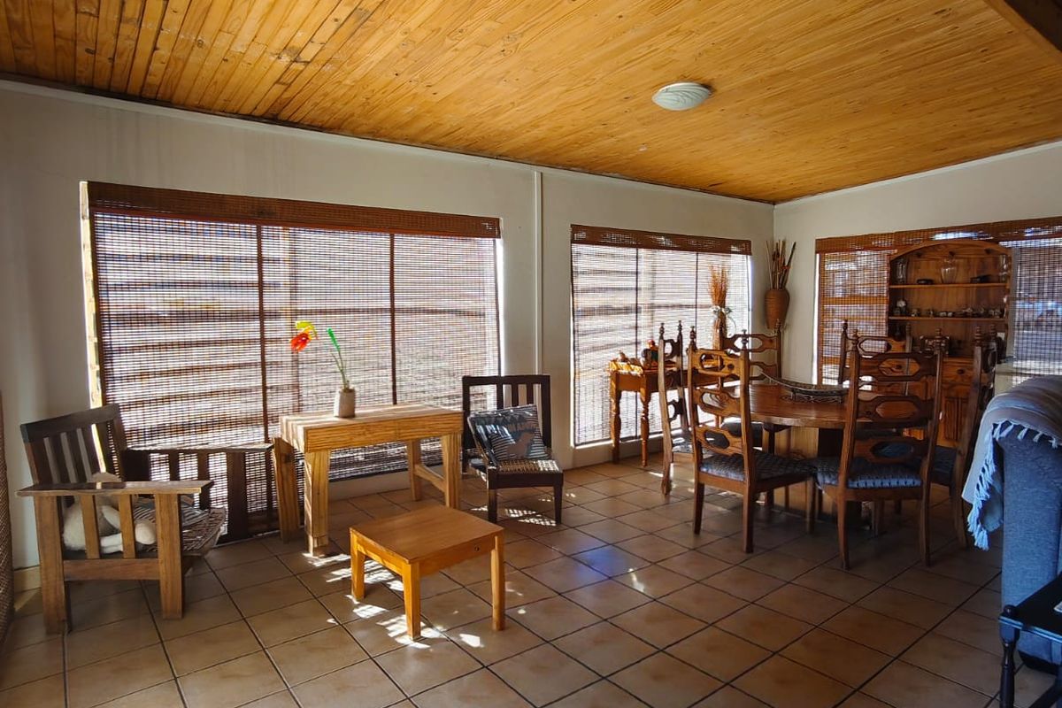 Spacious living area featuring a warm timber-clad ceiling with exposed beams and neutral ceramic floor tiles, complemented by natural bamboo window blinds.