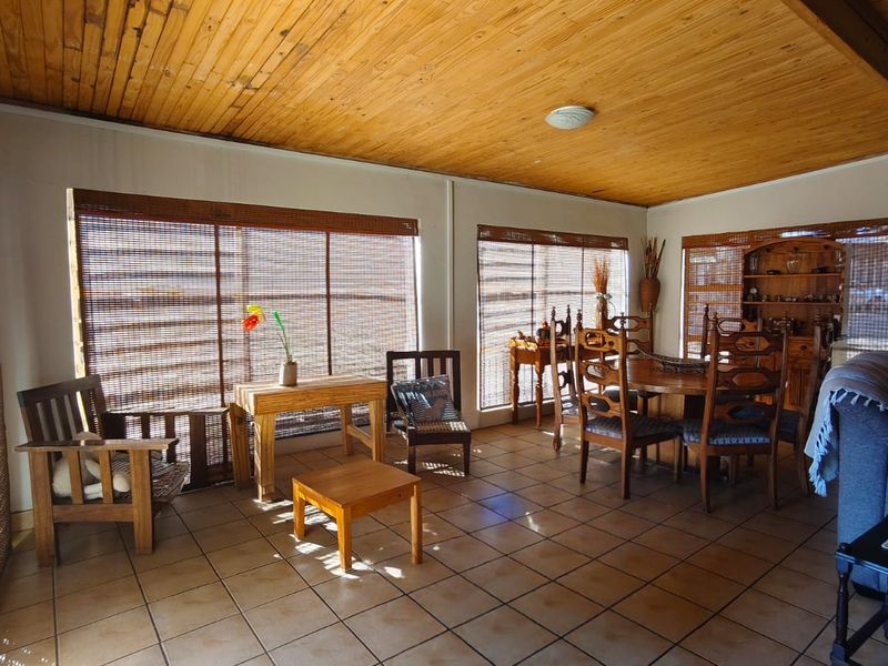 Spacious living area featuring a warm timber-clad ceiling with exposed beams and neutral ceramic floor tiles, complemented by natural bamboo window blinds.