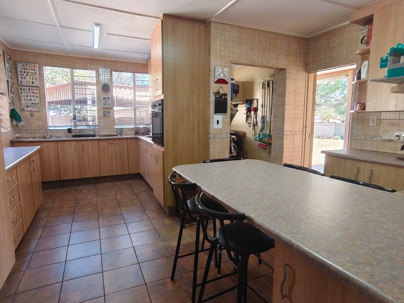 A functional kitchen featuring wood-look cabinetry, laminate countertops, built-in oven, and tiled flooring with direct access to an adjacent utility area.