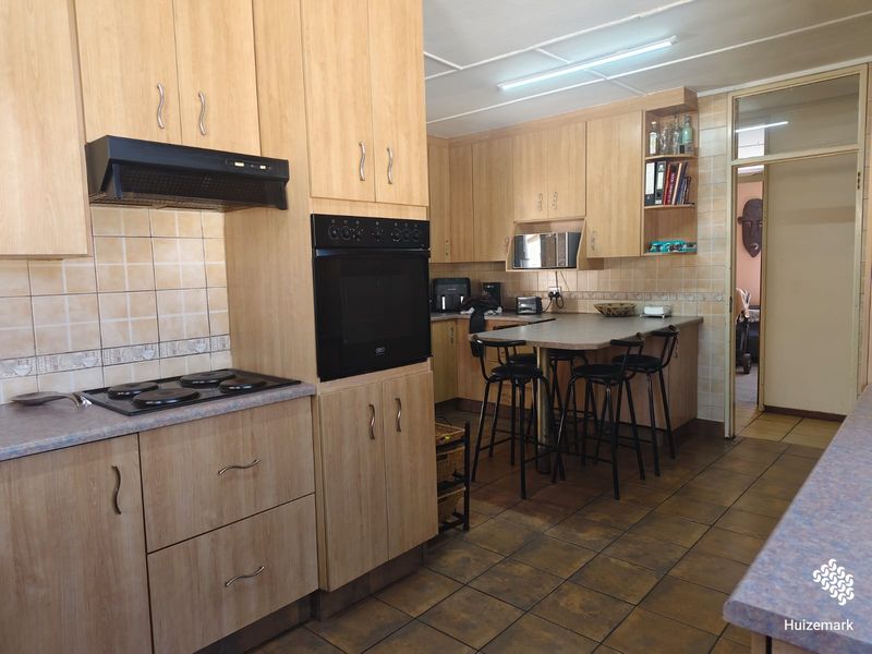 Functional kitchen featuring light wood-look cabinetry, built-in oven, electric hob, tiled backsplash, and a breakfast bar area with tiled flooring.