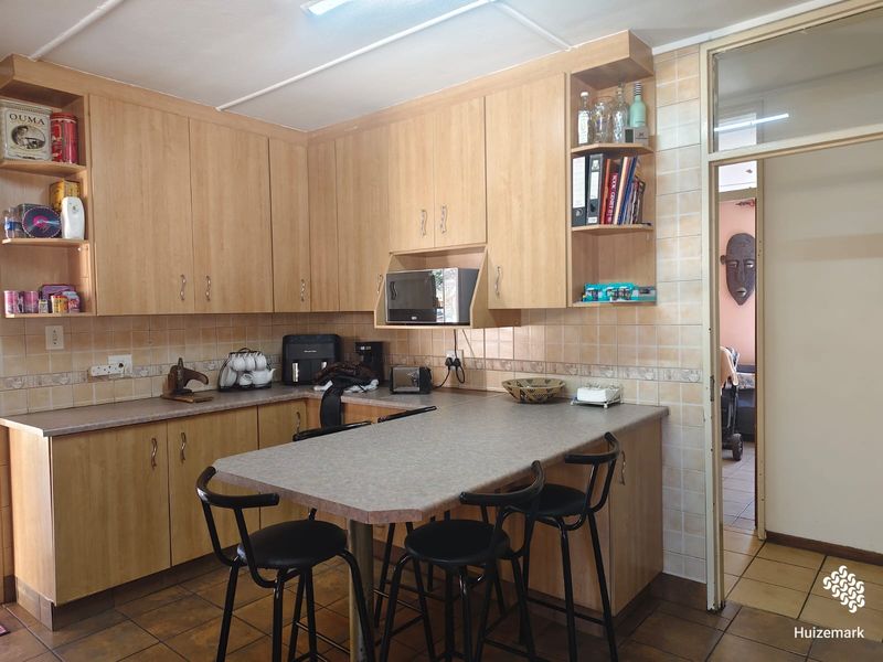 A functional kitchen featuring light wood-look cabinetry, laminate countertops with an integrated breakfast bar, and tiled finishes throughout.