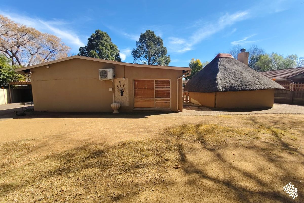 Rear view of the property featuring a traditional thatched roof lapa, paved outdoor area, and exterior wall-mounted air conditioning unit.