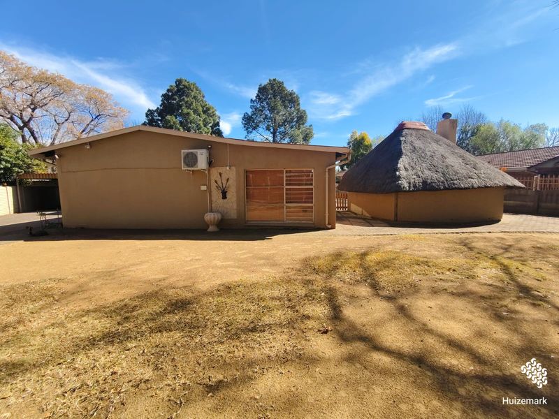 Rear view of the property featuring a traditional thatched roof lapa, paved outdoor area, and exterior wall-mounted air conditioning unit.