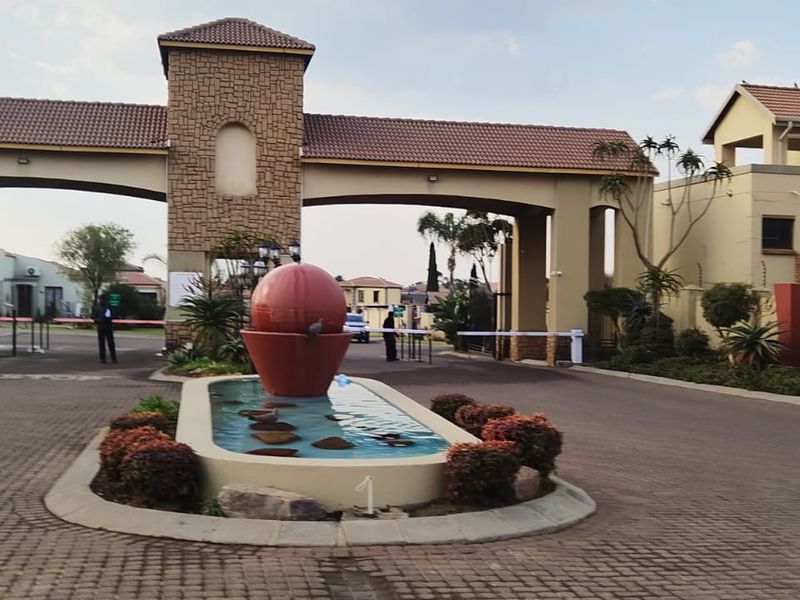 The main entrance to the residential estate featuring a secure gatehouse, paved driveway, and a decorative central water feature.