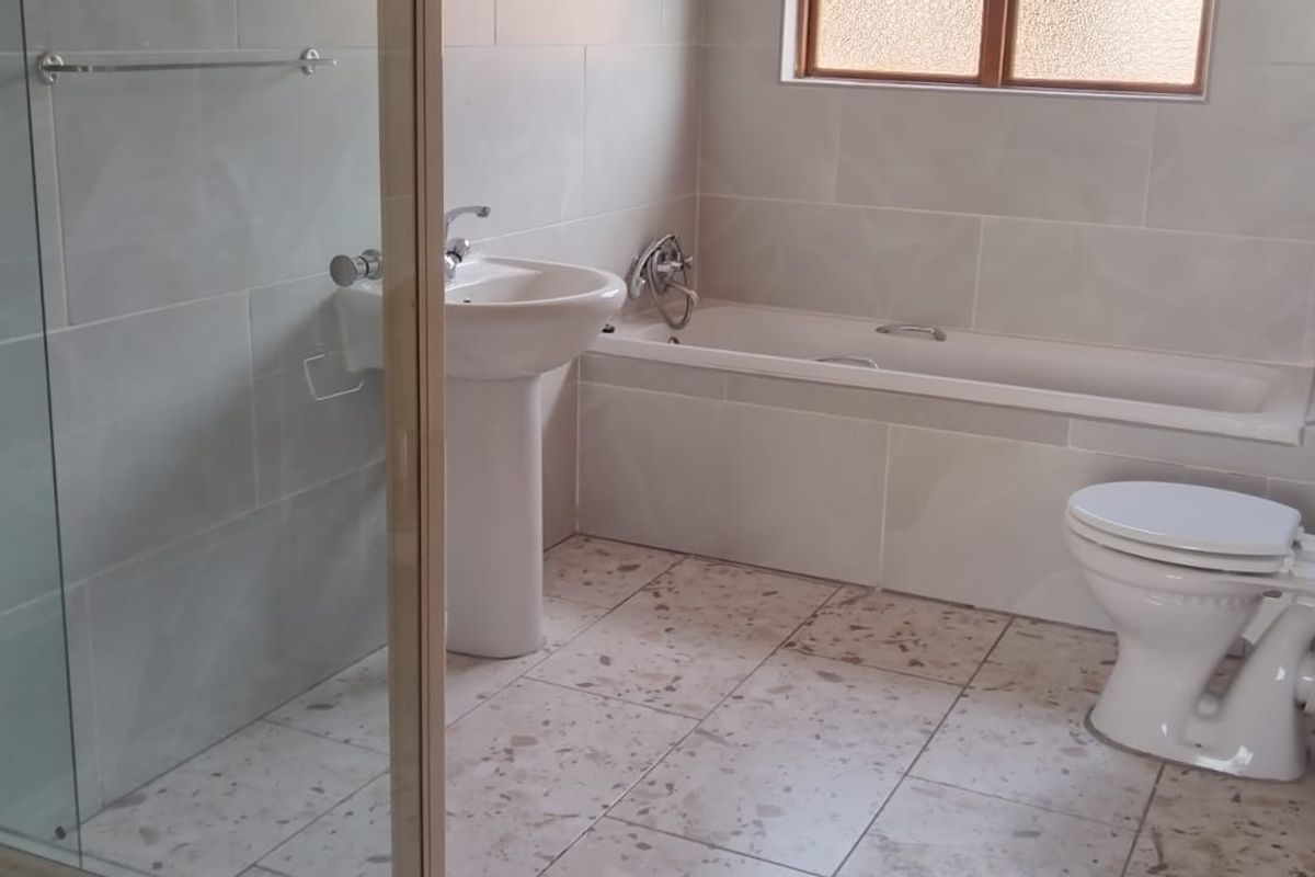 A functional bathroom featuring a pedestal basin, built-in bathtub, separate glass shower enclosure, and tiled finishes throughout.
