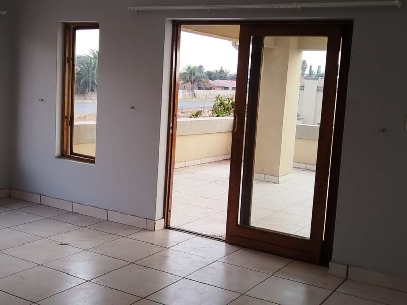 An empty living room featuring tiled flooring, wooden window frames, and a sliding glass door leading to an outdoor balcony area.