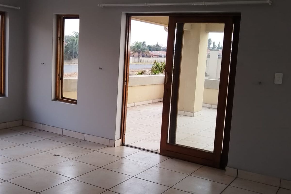 An empty living room featuring tiled flooring, wooden window frames, and a sliding glass door leading to an outdoor balcony area.