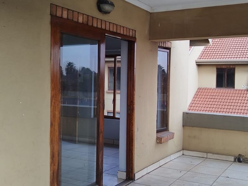 A covered balcony area featuring tiled flooring and sliding glass door access to the interior, showing signs of wear on the exterior finishes.