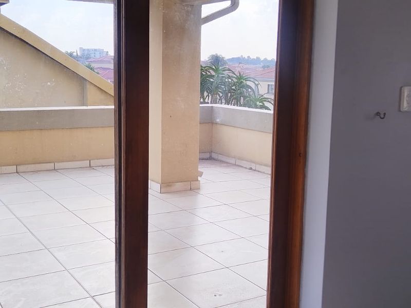 A spacious penthouse balcony featuring tiled flooring, a concrete balustrade, and sliding glass door access, offering an open outdoor area.