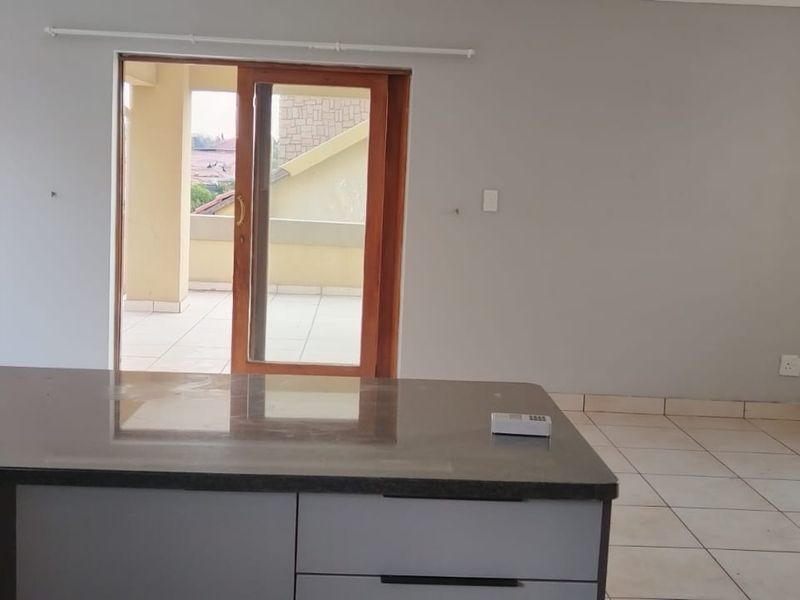 Open plan living area featuring a kitchen island with granite countertop, tiled flooring, and direct access to a private balcony through sliding glass doors.