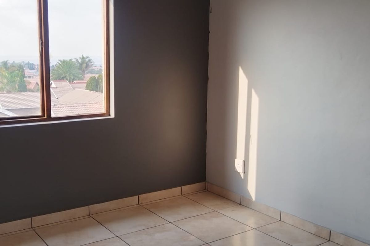 An empty bedroom featuring tiled flooring, neutral wall tones, and a window providing natural light and neighborhood views.