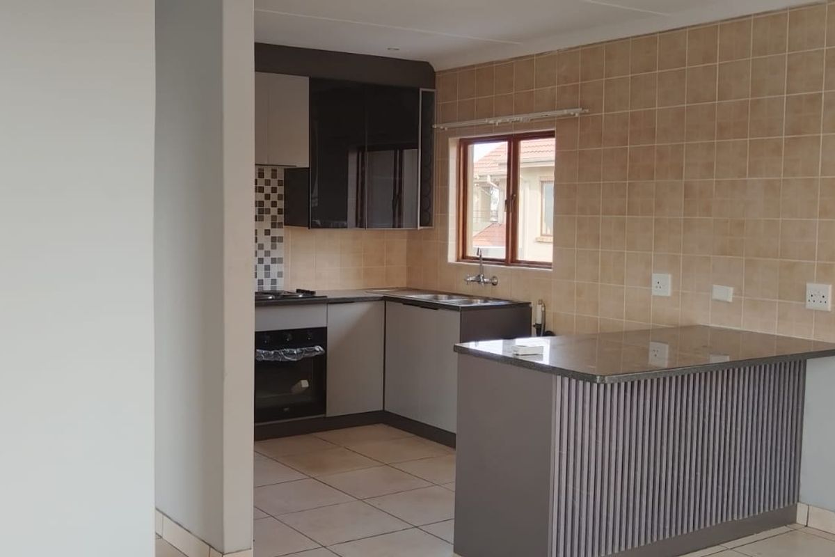 A functional kitchen featuring modern cabinetry, a stone breakfast bar, built-in oven, hob, and tiled backsplash, offering a clean and practical workspace.