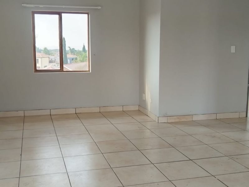 An empty open-plan living area featuring tiled flooring, a window with exterior views, and a breakfast bar connecting to the kitchen space.