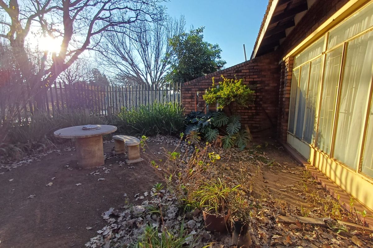 A rear exterior view of the townhouse featuring a brick facade, sliding glass doors, and a garden area with metal security fencing.