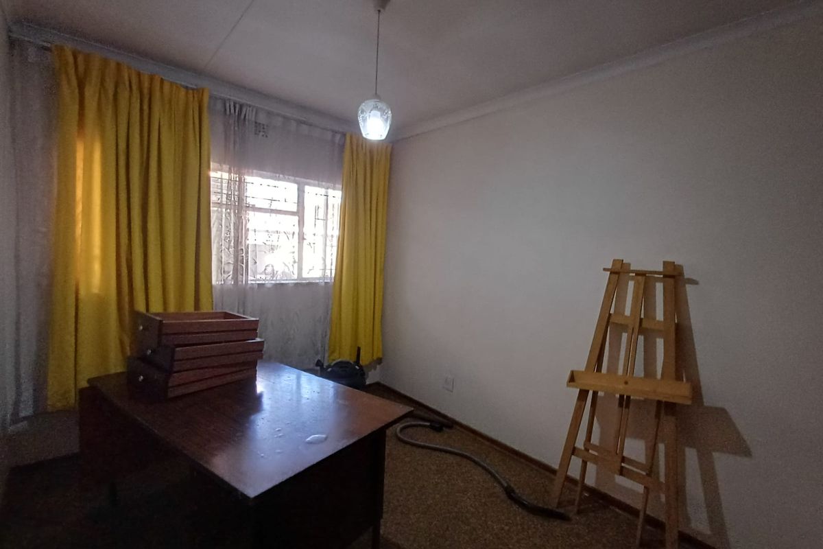 A simple bedroom featuring carpet flooring, window security bars, and a central pendant light fixture, offering a blank canvas for renovation.