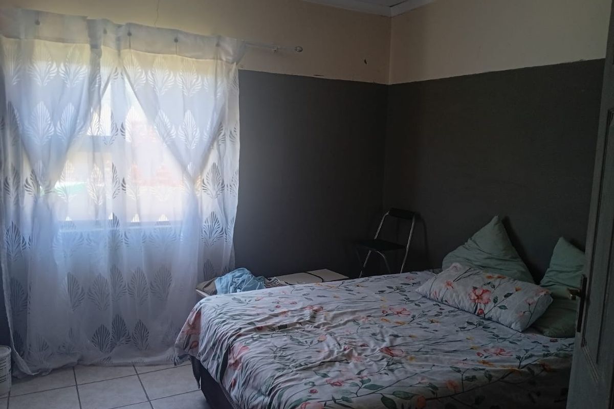 A bedroom featuring tiled flooring and two-tone wall paint, showing visible signs of plaster cracking near the ceiling.