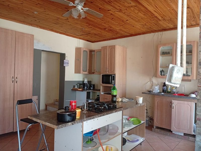 A dated kitchen featuring timber ceilings, tiled floors, and a central island with a gas hob, requiring cosmetic updates and finishing work.