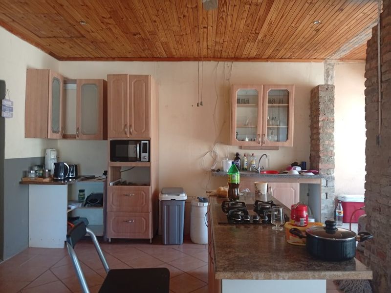 Kitchen featuring timber ceiling, built-in cabinetry, gas hob, and stone countertops, with an exposed brick pillar and tiled flooring.
