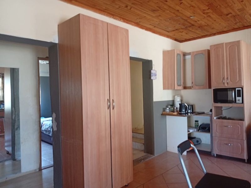 A kitchen area featuring timber ceiling panels, tiled flooring, and built-in cabinetry with integrated microwave housing, showing signs of wear and dated finishes.